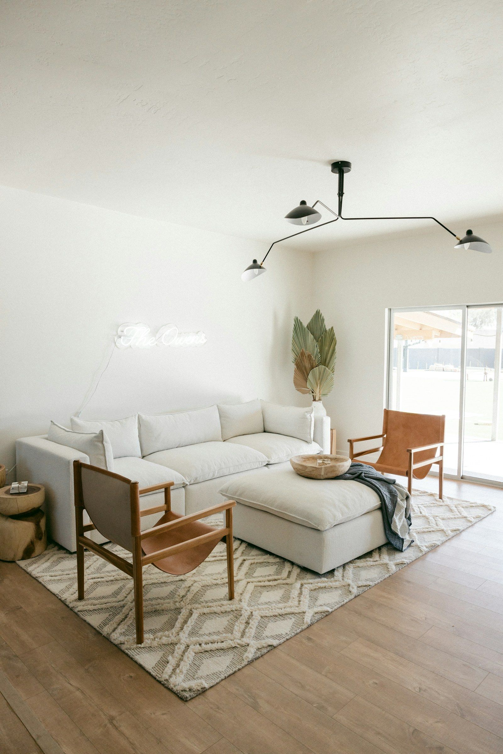 A bright living room with a white sectional, a leather sling chair and a patterned rug in afternoon light.
