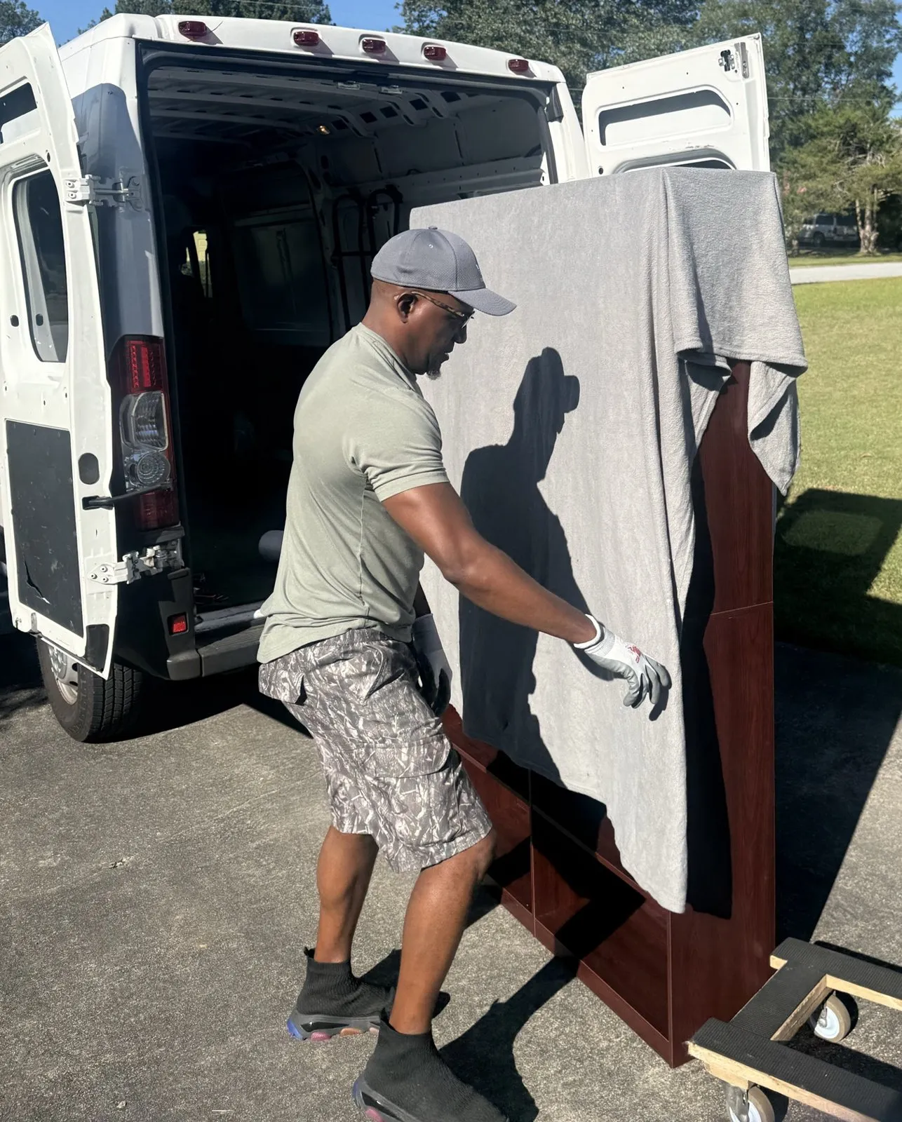 Jack draping a moving blanket over a tall wooden bookcase on a dolly beside the open van.