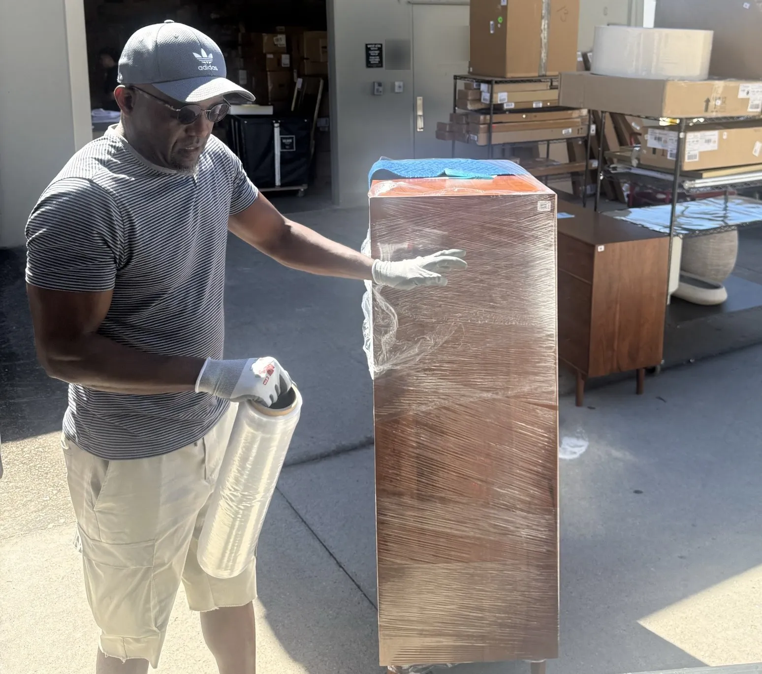 Jack shrink-wrapping a dresser at a furniture store pickup dock before loading it.